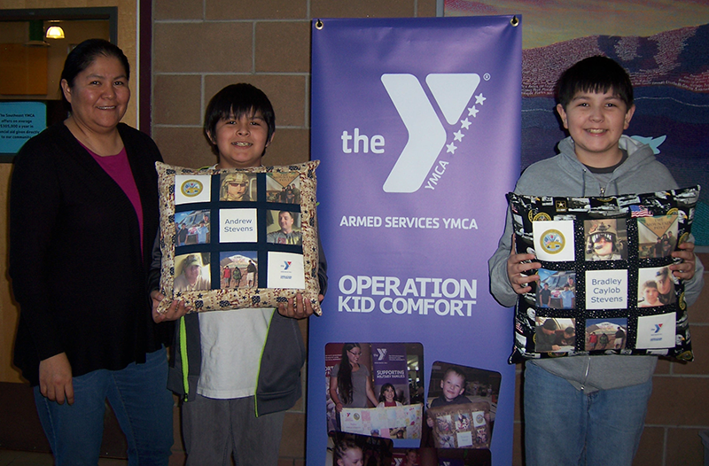 A woman and two young boys posing in front of a YMCA operation kid comfort flag