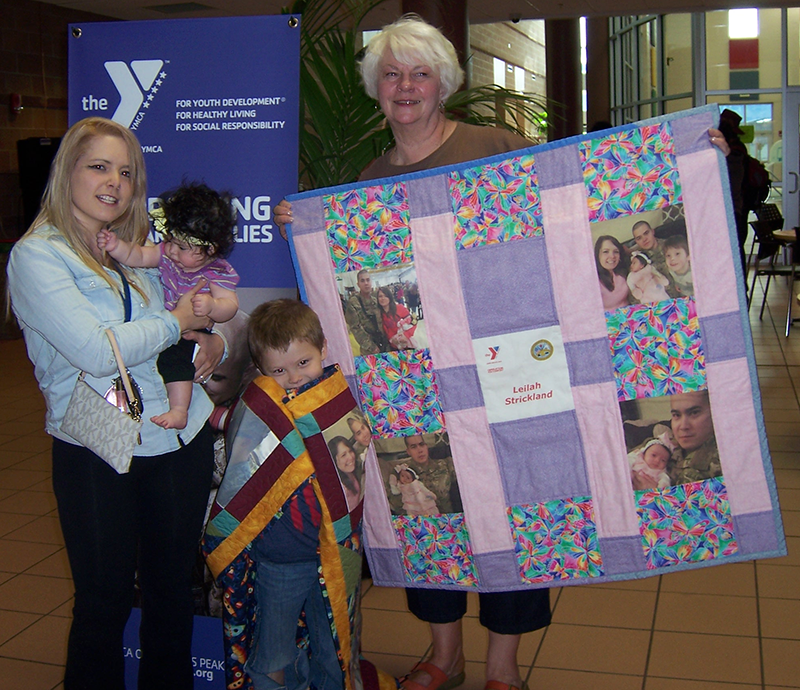 Two women and two children posing in front of a YMCA operation kid comfort flag